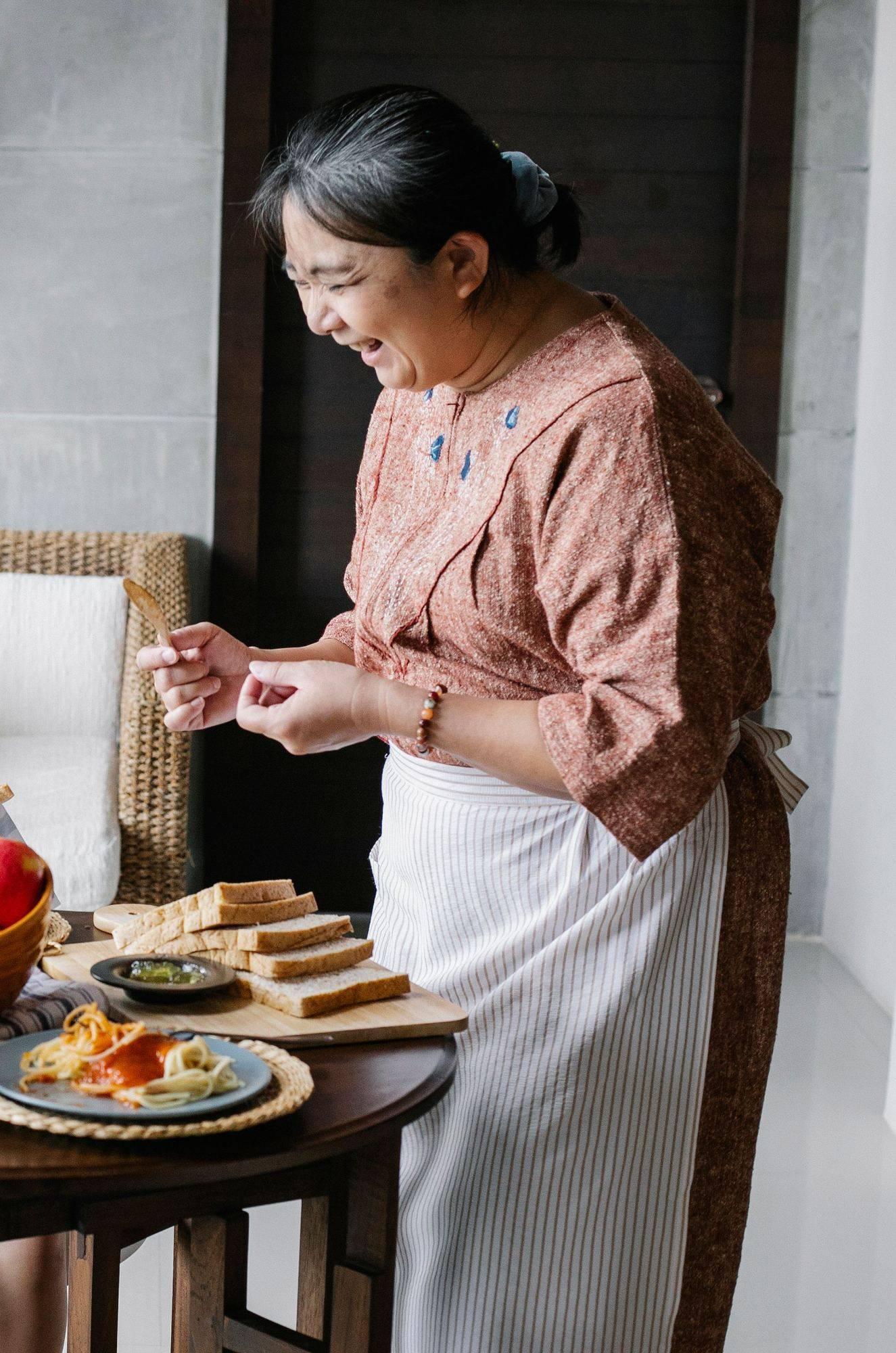 An older woman smiling as she sets out a home-cooked meal in her kitchen.